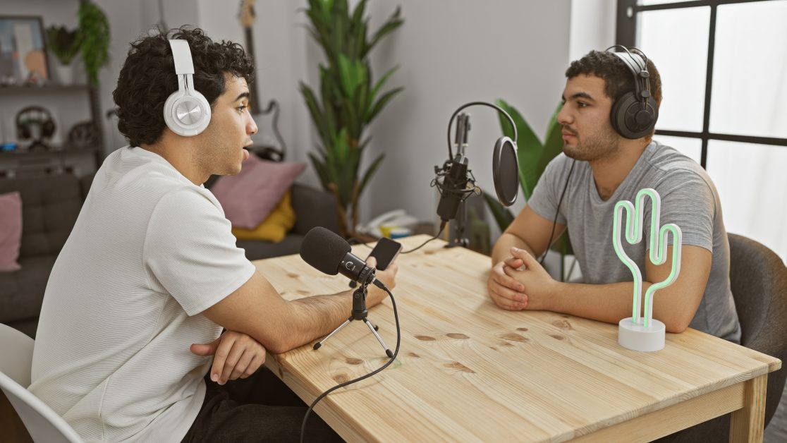 Two men podcasting in a modern home studio with headphones and microphones.